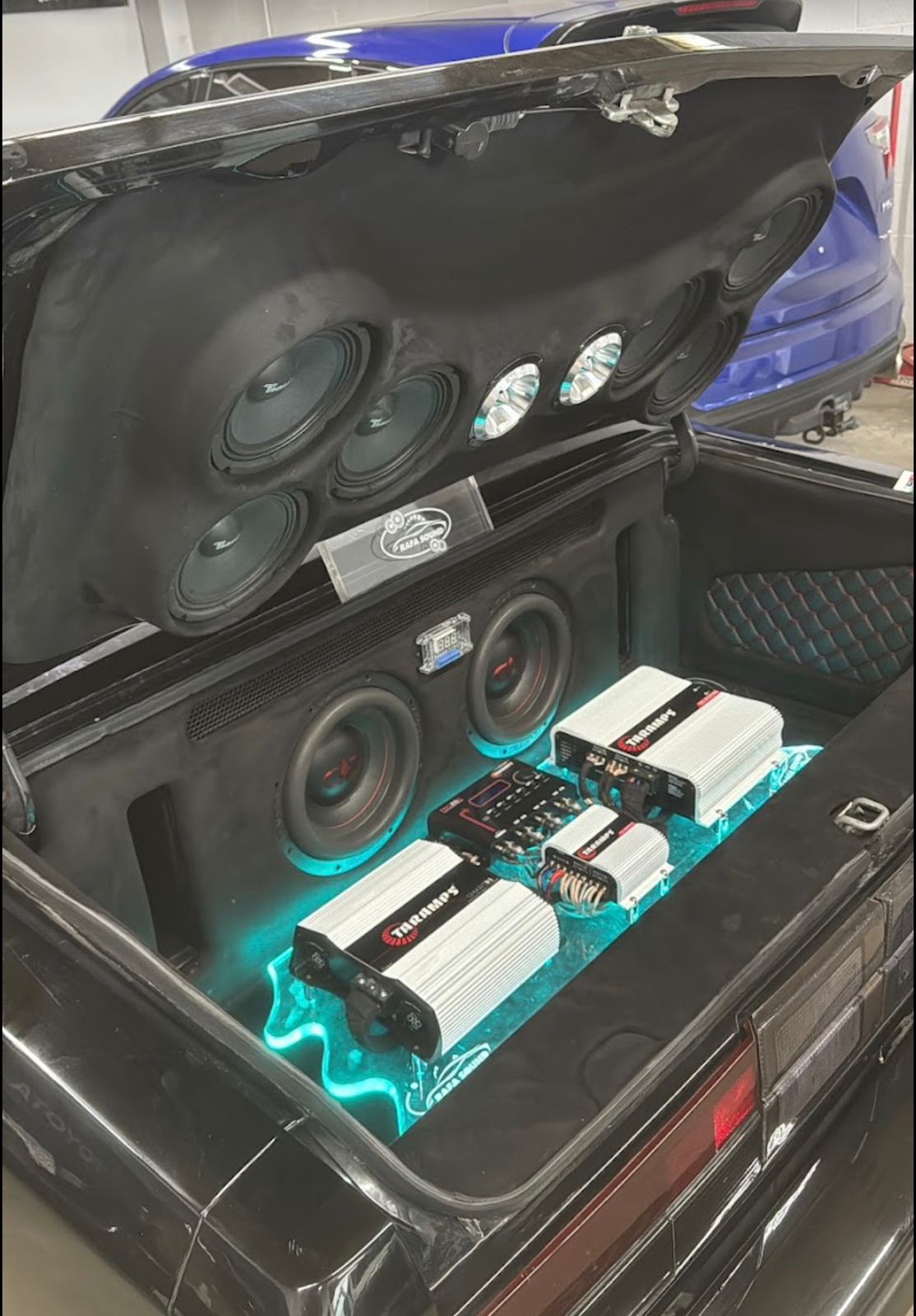 Full custom trunk build in a black car with a speaker wall, subwoofers and teal lighting